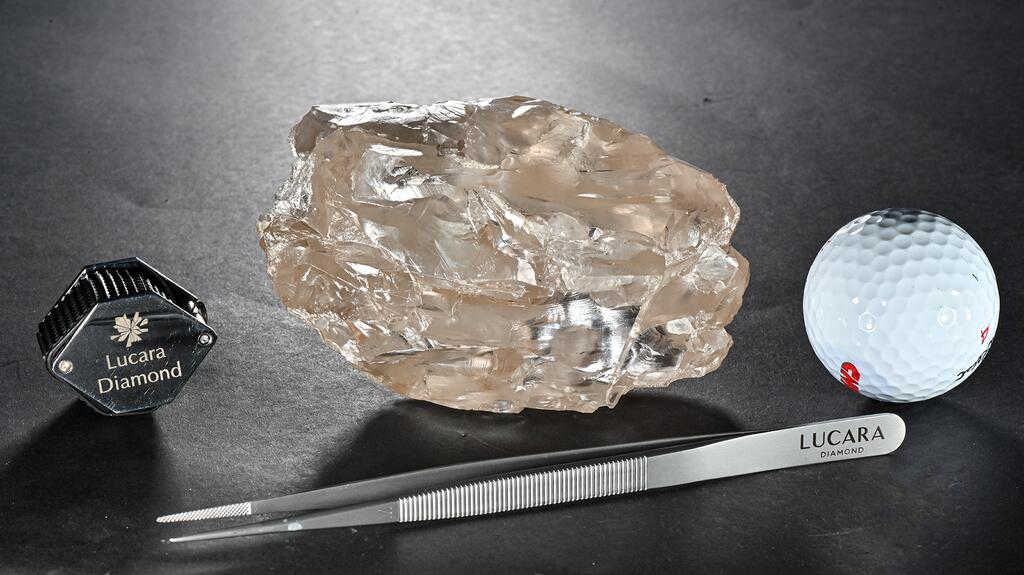 The 2,492-carat rough diamond is shown alongside a loupe, a pair of tweezers, and a golf ball for scale. 2492-carat rough diamond from Karowe mine